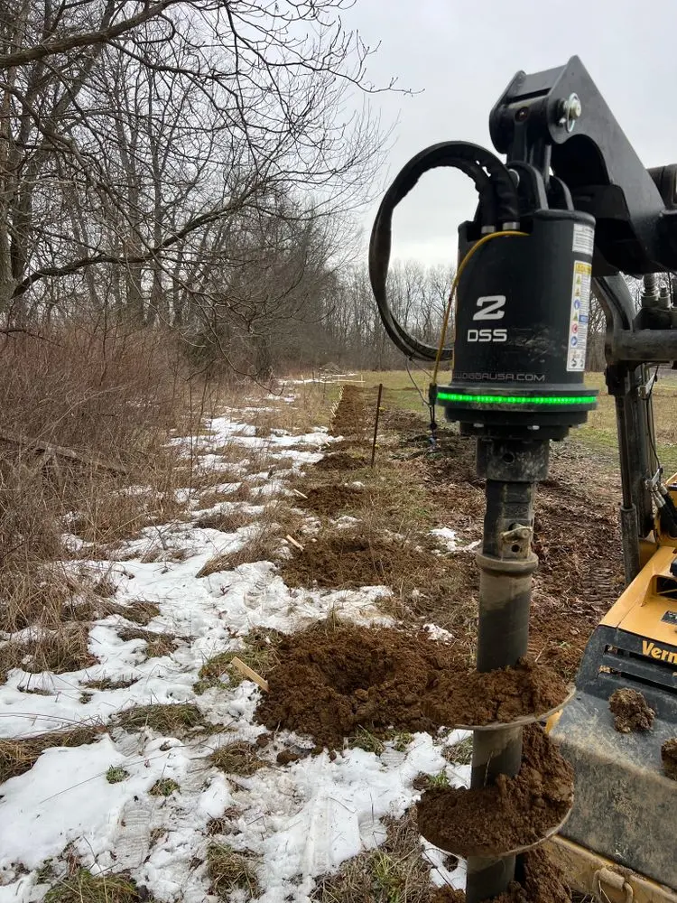 Auger drilling fence postholes in snowy winter conditions along a fence line in Michigan