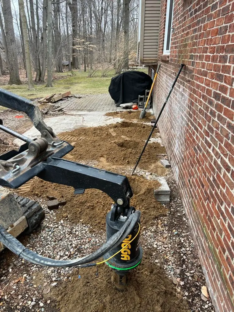 Auger equipment drilling postholes next to a brick house for deck or fence foundation